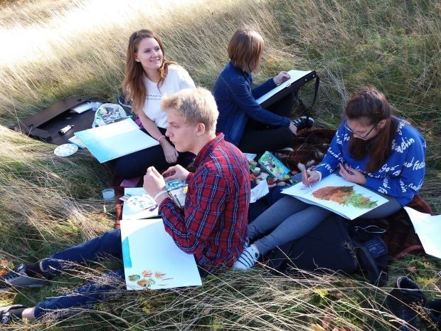 cztery młode dziewczyny siedzą na trawie i malują