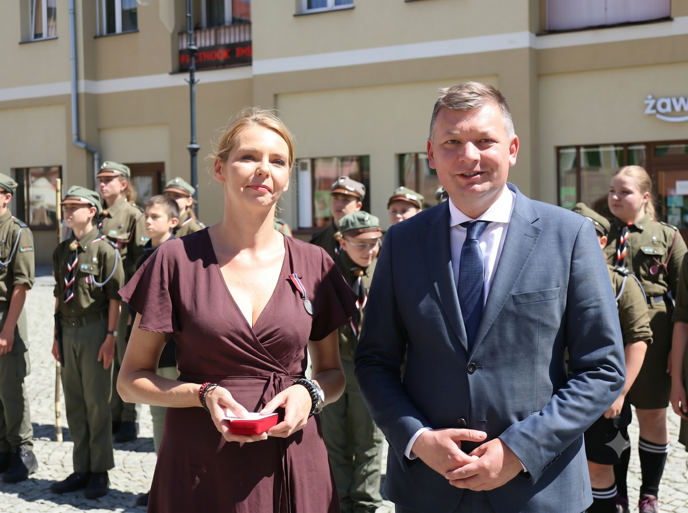 Po lewej kobieta z medalem, po prawej mężczyzna w marynarce. Widoczni do połowy