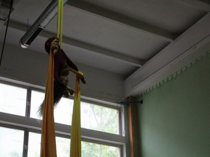 Dziewczyna dokonuje akrobacji na taśmie podwieszonej do sufitu sali sportowej