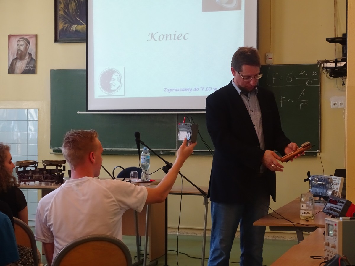 Wykładowca stoi na tle ekrany, siedzący przed nim uczeń robi mu zdjęcie telefonem komórkowym