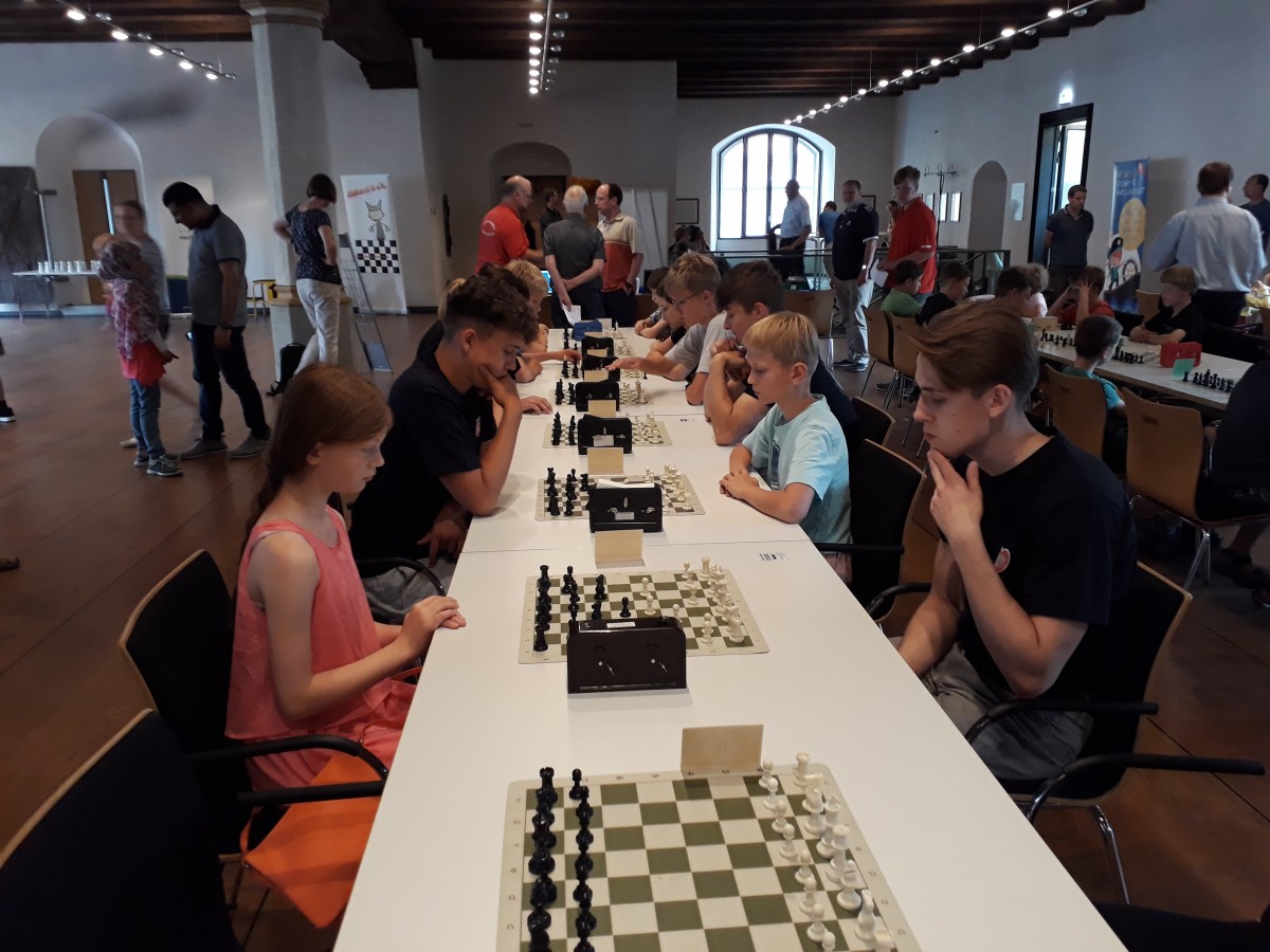 Młodzież podczas szachowych zawodów. Siedzą przy stolikach, przy szachownicach.