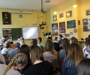 Widać głowy i tułowia dwudziestu kilku uczniów, od tyłu. Uczniowie siedzą. W tle widać ściany ozdobione plakatami z widokami kosmosu.