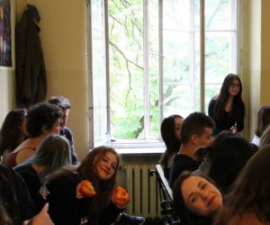 Widać siedzących uczniów, kilkunastu, dziewcząt i chłopców. Jedna dziewczyna siedzi na parapecie okna.